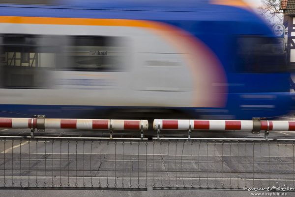 vorbeifahrender Zug, davor geschlossene Schranken eines Bahnübergangs, Cantus, Bahnübergang Friedland, Friedland, Deutschland