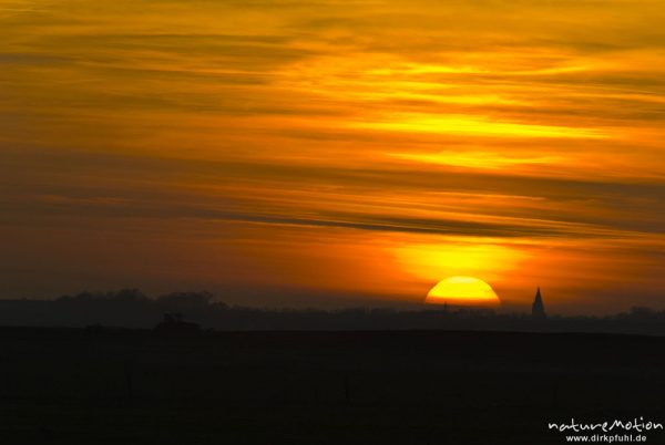 untergehende Sonne und Abendrot, Silhouette der Marienkirche von Barth, Traktor fährt im Vordergrund über Acker, Günzer Wiesen, Groß Mohrdorf, Deutschland