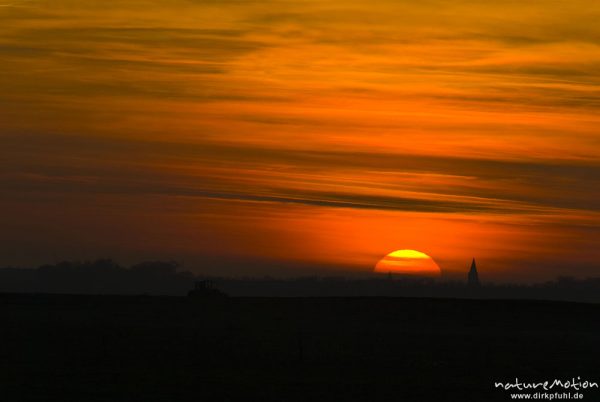 untergehende Sonne und Abendrot, Silhouette der Marienkirche von Barth, Traktor fährt im Vordergrund über Acker, Günzer Wiesen, Groß Mohrdorf, Deutschland