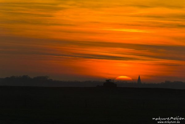 untergehende Sonne und Abendrot, Silhouette der Marienkirche von Barth, Traktor fährt im Vordergrund über Acker, Günzer Wiesen, Groß Mohrdorf, Deutschland