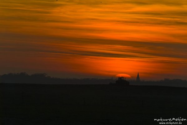 untergehende Sonne und Abendrot, Silhouette der Marienkirche von Barth, Traktor fährt im Vordergrund über Acker, Günzer Wiesen, Groß Mohrdorf, Deutschland