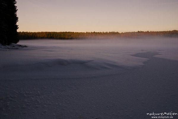 Nebel über dem zugefrorenen Oderteich, letztes Tageslicht, vom Sonnenuntergang orange gefärbt, Eiskristalle, Schneeverwehungen, Harz, Torfhaus, Deutschland