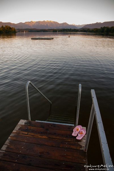 Steg mit Badelatschen, See mit Bergpanorma im Abendlicht, Strandbad Uffing, Staffelsee, Deutschland