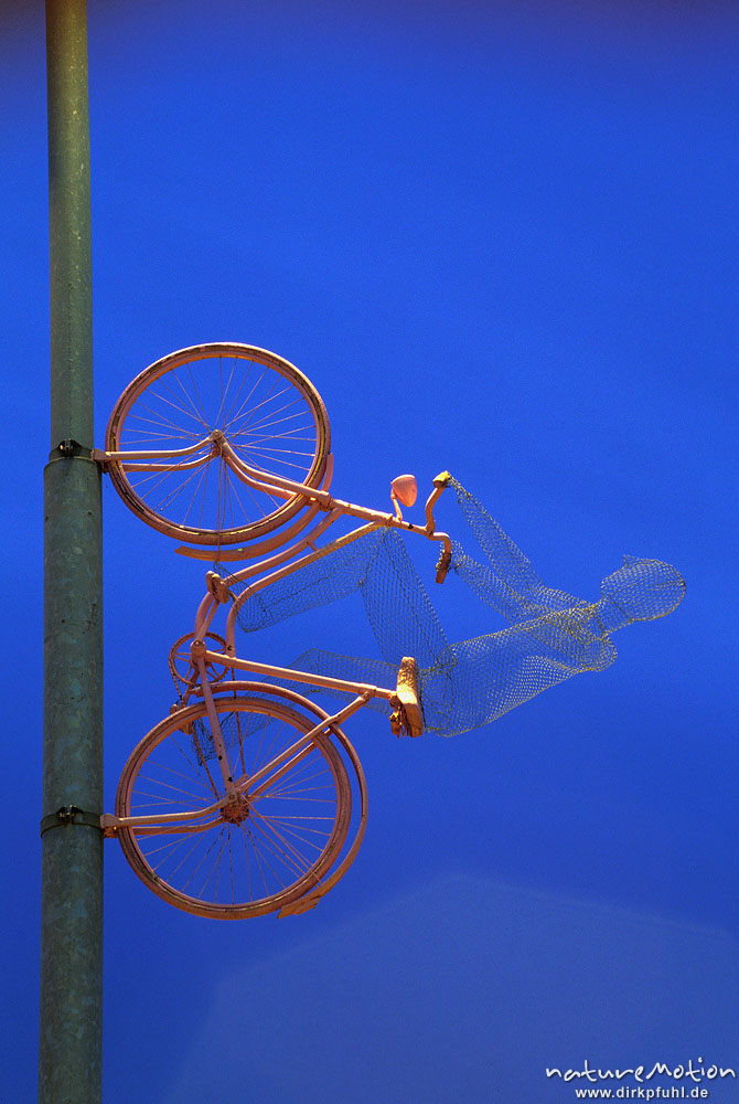 Fahrrad mit Fahrer aus Draht, senkrecht an Lichtmast