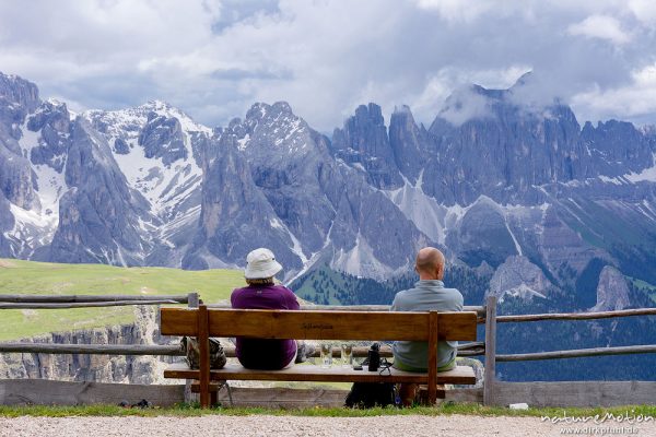 Mann und Frau sitzen auf Bank vor Bergpanorama, Rosengarten, Dolomiten, Schlernhaus, Seiseralm (Südtirol), Italien