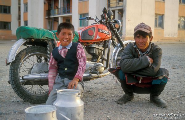 Airag-Verkäufer, Vater und Sohn mit Milchkannen vor ihrem Motorrad, im Hintergrund Plattenbauten, Chowd, Mongolei