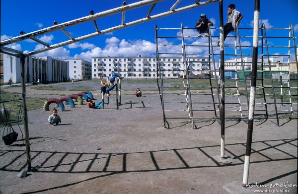 Spielplatz mit verbogenem Klettergerüst hinter Plattenbauten, turnende Kinder, Ulaanbaatar – Ulan Bator, Mongolei