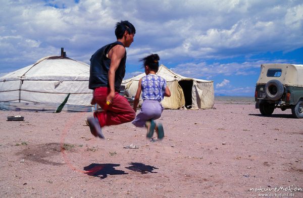 Zeitvertreib am Nachmittag, Junge und Mädchen beim Seilspringen vor Jurte, Wüste Gobi, Mongolei