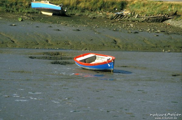 rot-blaues Ruderboot liegt auf trocken gefallenem Schlick im Hafenbecken, Bretagne, Frankreich